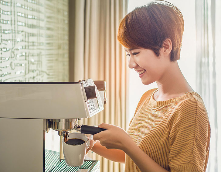 エスプレッソマシンでコーヒーを淹れる若い女性