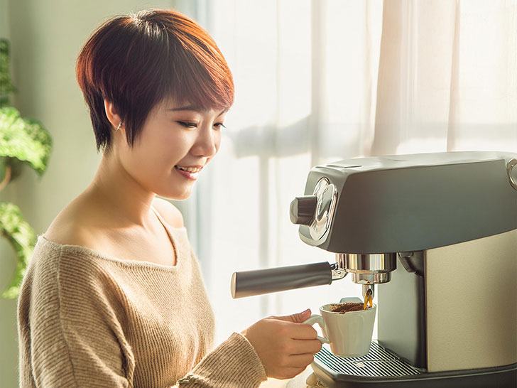 エスプレッソマシンでコーヒーを淹れる若い女性