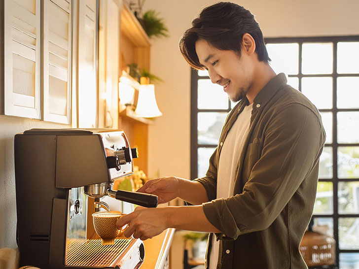 エスプレッソマシンでコーヒーを淹れる若いオシャレな男性