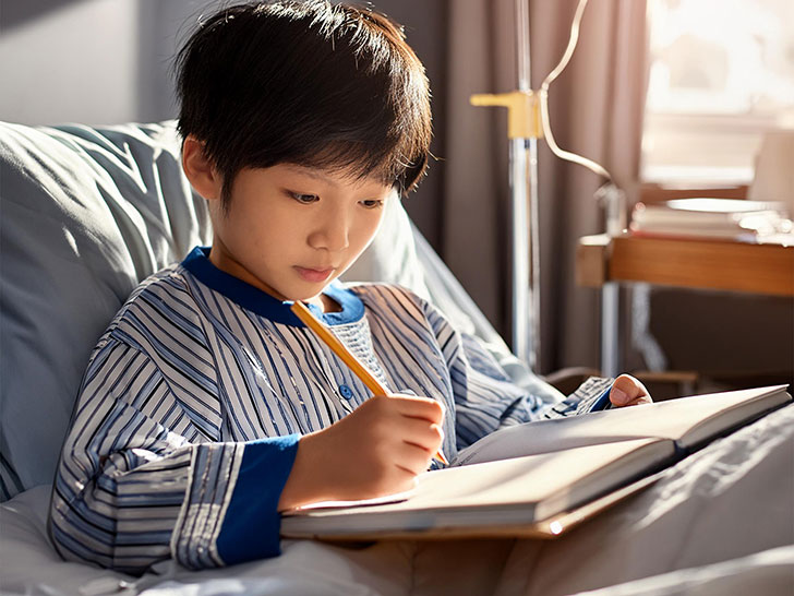 病院のベッドで勉強する小学生の男の子