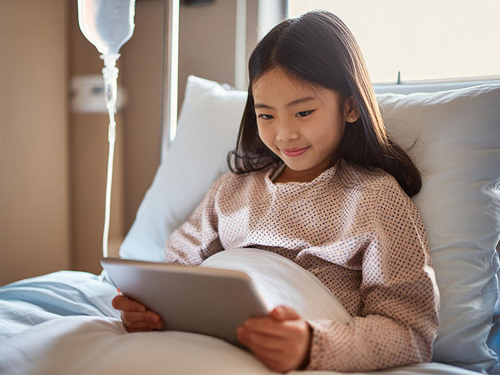 病院のベッドでタブレットを見る小学生の女の子