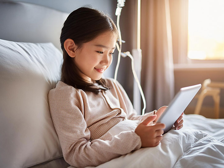 病院のベッドでタブレットを見る小学生の女の子