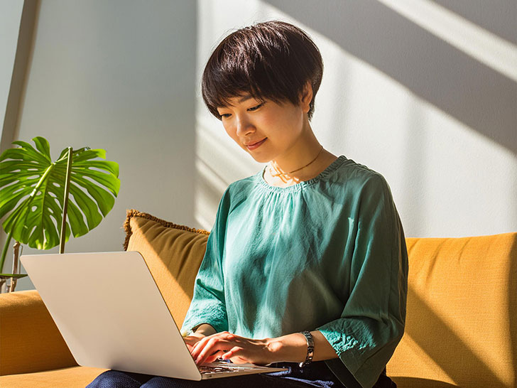 ソファに座ってノートパソコンで仕事をする女性