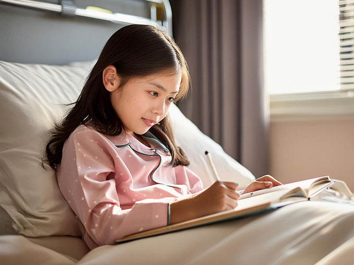 病院のベッドで勉強する小学生の女の子