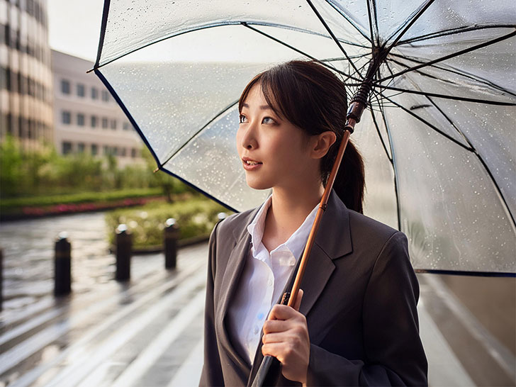 スーツを着て雨傘をさす若い女性