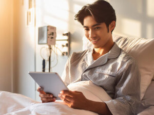 病院のベッドでタブレットを見る若い男性