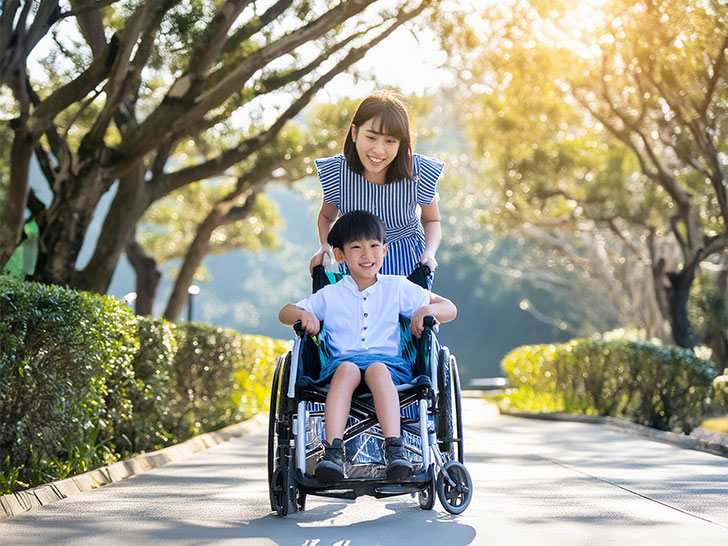 小さな息子の車椅子を押すお母さん