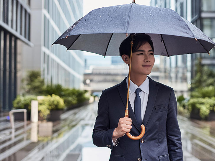 スーツを着て雨傘をさす若い男性