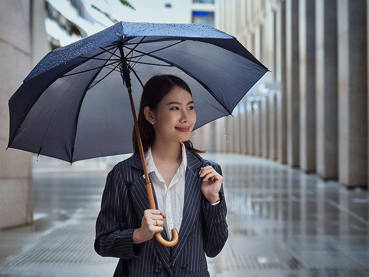 スーツを着て雨傘をさす若い女性