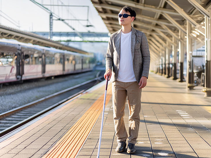 白杖をついて駅のホームを歩く男性