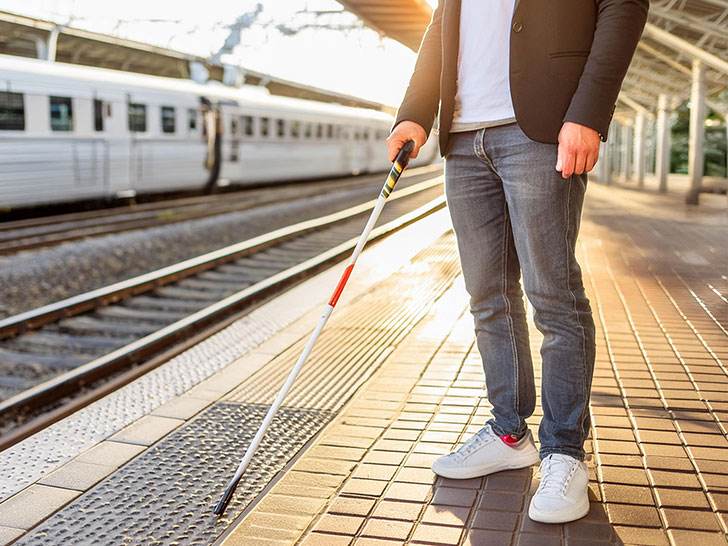 駅のホームを歩く視覚障がい者の男性の足元