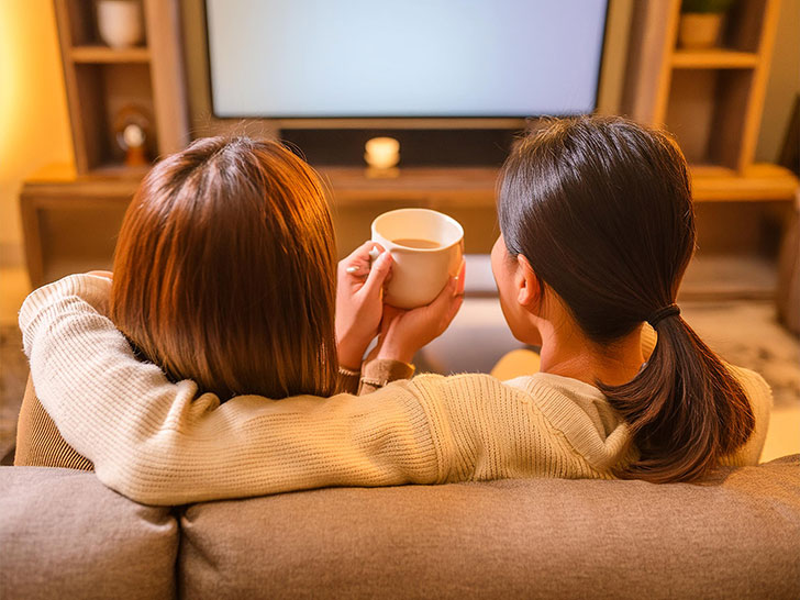 ソファに並んで座る女性カップルの後ろ姿