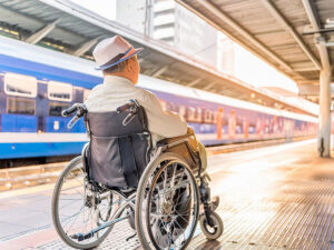 車椅子で駅のホームに佇む高齢男性