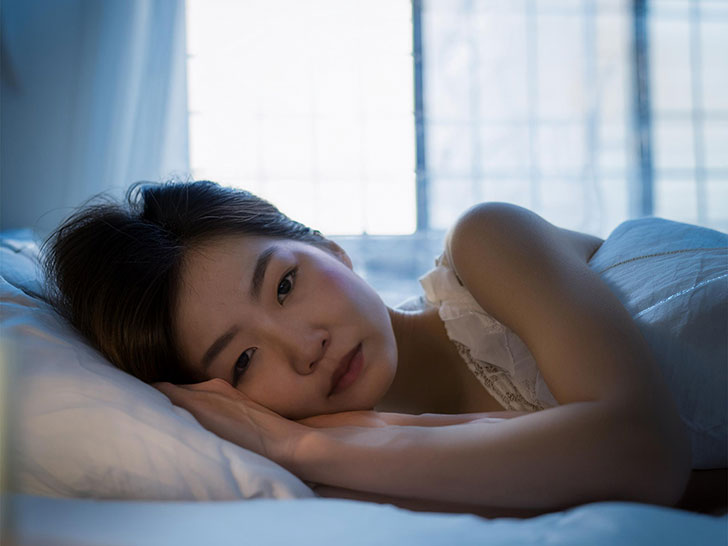 ベッドに横たわって眠れずにいる若い女性