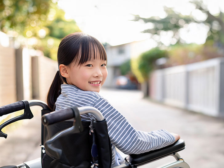 車椅子に座り笑顔を見せる小学生の女の子