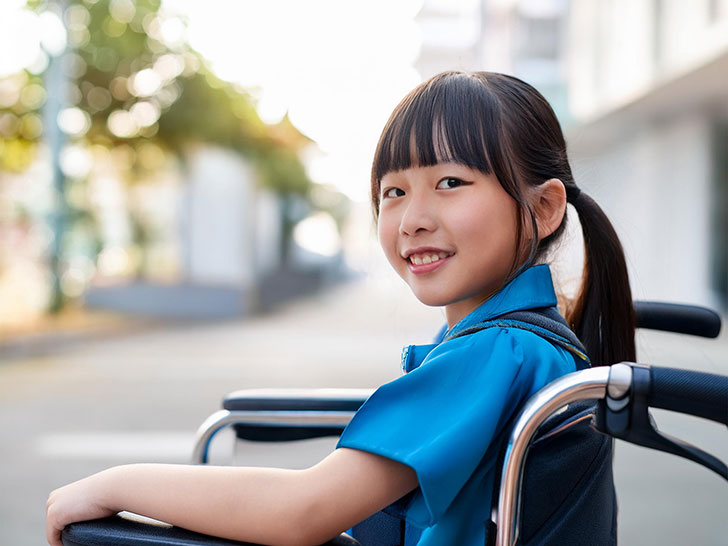 車椅子に座り笑顔を見せる小学生の女の子