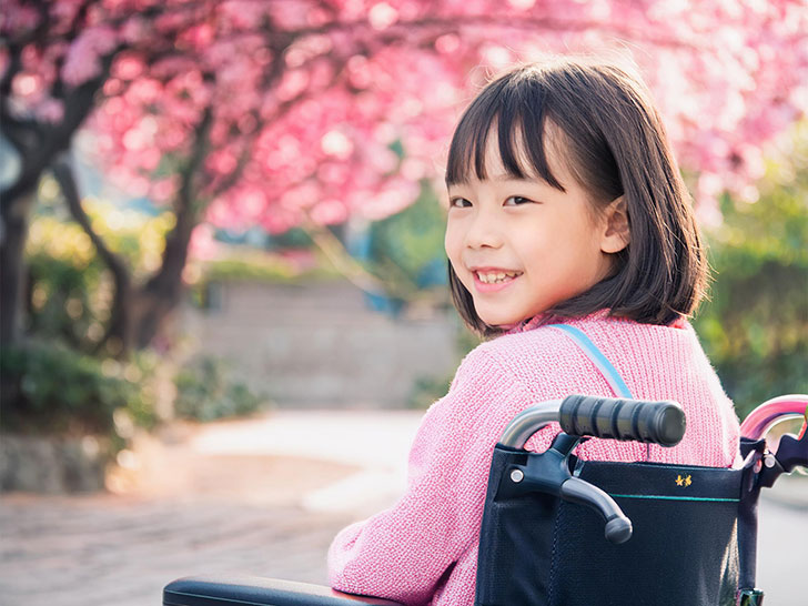 車椅子に座り笑顔を見せる小学生の女の子