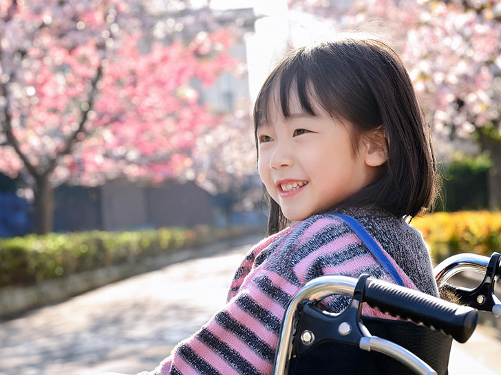 車椅子に座り笑顔を見せる小学生の女の子