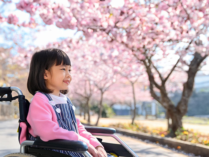 車椅子に座り笑顔を見せる小学生の女の子