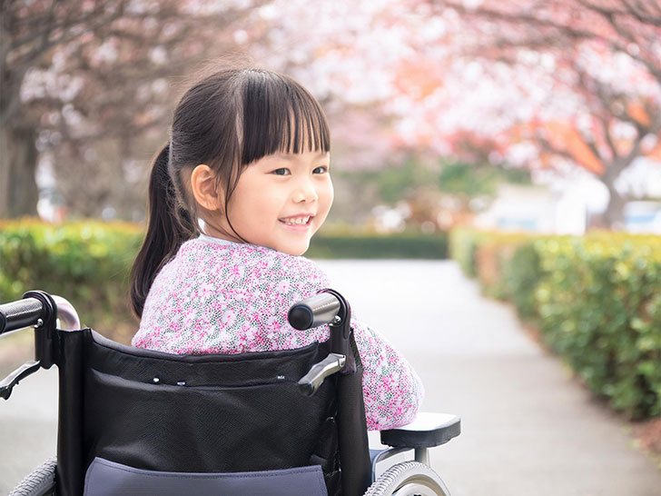 車椅子に座り笑顔を見せる小学生の女の子