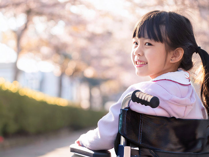 車椅子に座り笑顔を見せる小学生の女の子