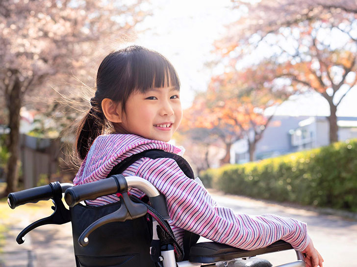 車椅子に座り笑顔を見せる小学生の女の子