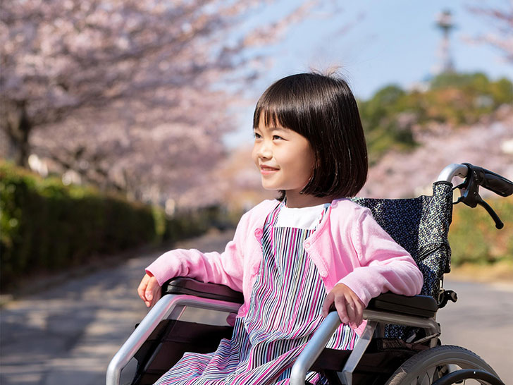 車椅子に座り笑顔を見せる小学生の女の子