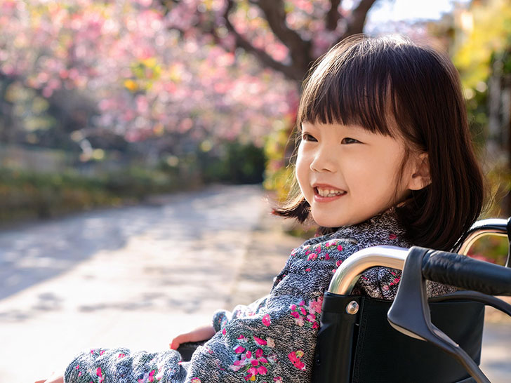 車椅子に座り笑顔を見せる小学生の女の子