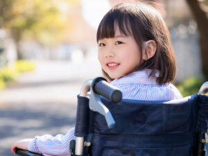 車椅子に座り笑顔を見せる小学生の女の子