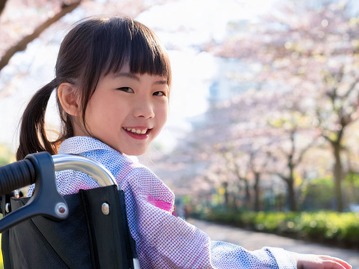 車椅子に座り笑顔を見せる小学生の女の子