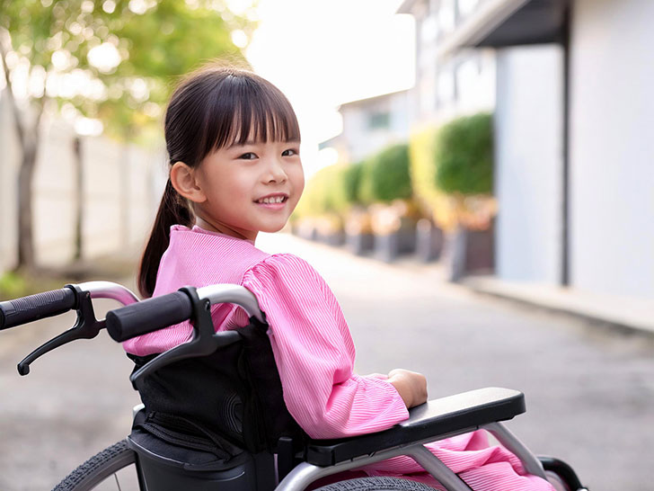 車椅子に座り笑顔を見せる小学生の女の子