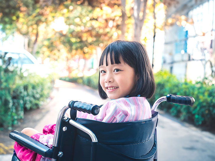 車椅子に座り笑顔を見せる小学生の女の子