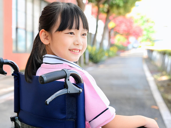 車椅子に座り笑顔を見せる小学生の女の子