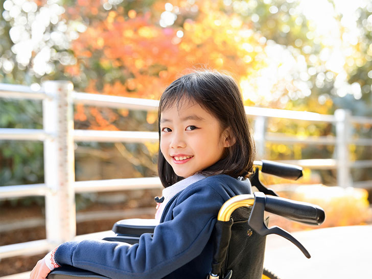 車椅子に座り笑顔を見せる小学生の女の子