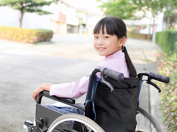 車椅子に座り笑顔を見せる小学生の女の子