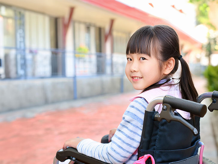 車椅子に座り笑顔を見せる小学生の女の子