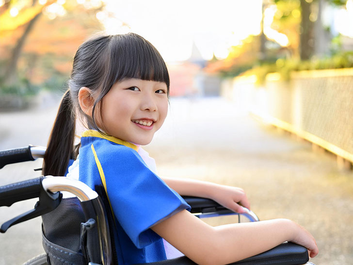 車椅子に座り笑顔を見せる小学生の女の子