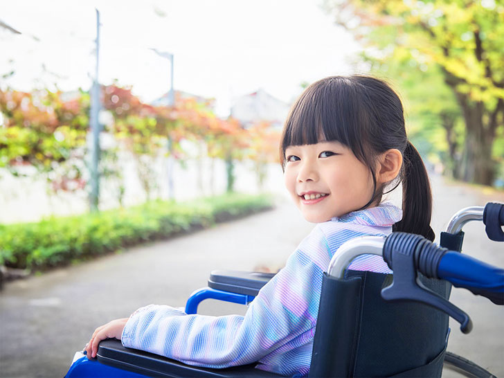 車椅子に座り笑顔を見せる小学生の女の子