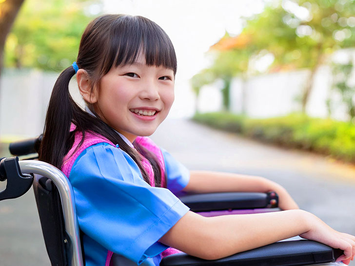 車椅子に座り笑顔を見せる小学生の女の子