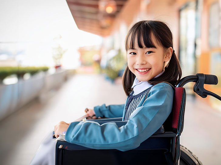 車椅子に座り笑顔を見せる小学生の女の子