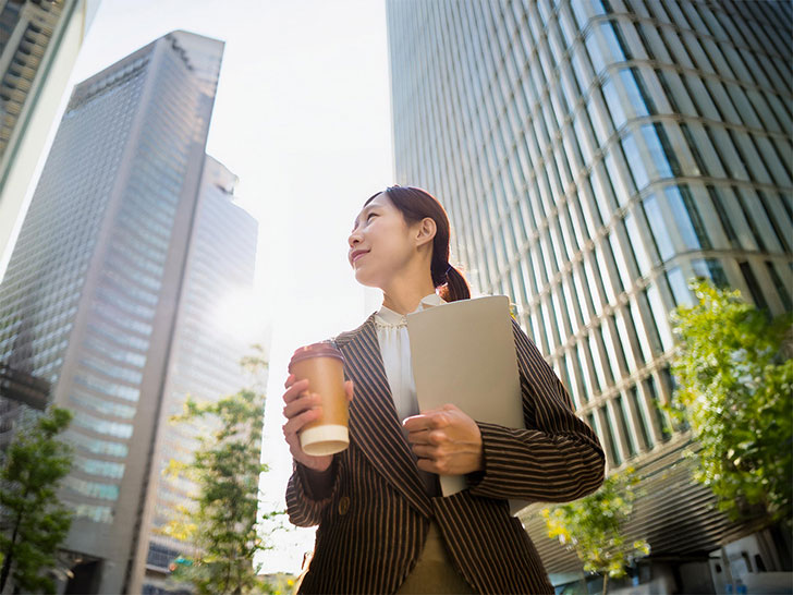 コーヒーを片手にオフィス街にたたずむ女性