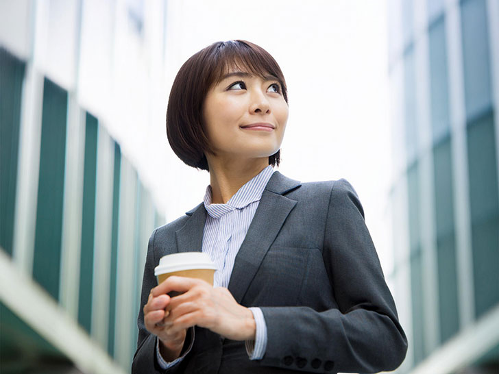 コーヒーを片手にオフィス街にたたずむ女性