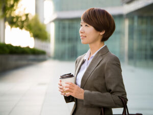 コーヒーを片手にオフィス街にたたずむ女性