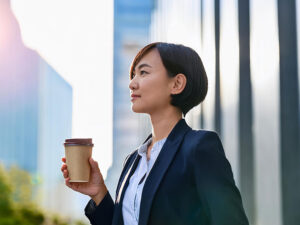 コーヒーを片手にオフィス街にたたずむ女性