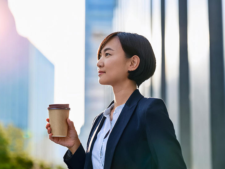 コーヒーを片手にオフィス街にたたずむ女性