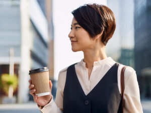 コーヒーを片手にオフィス街にたたずむ女性