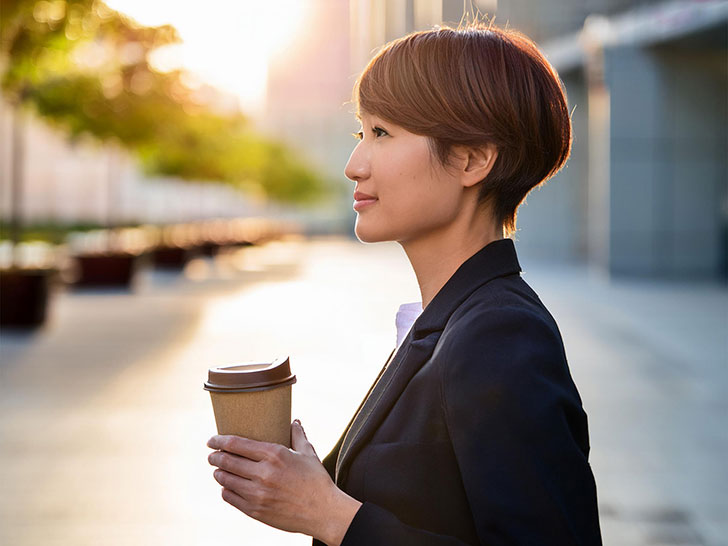 コーヒーを片手にオフィス街にたたずむ女性