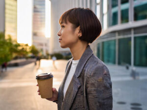 コーヒーを片手にオフィス街にたたずむ女性