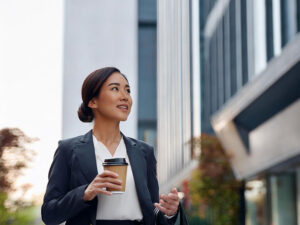 コーヒーを片手にオフィス街にたたずむ女性