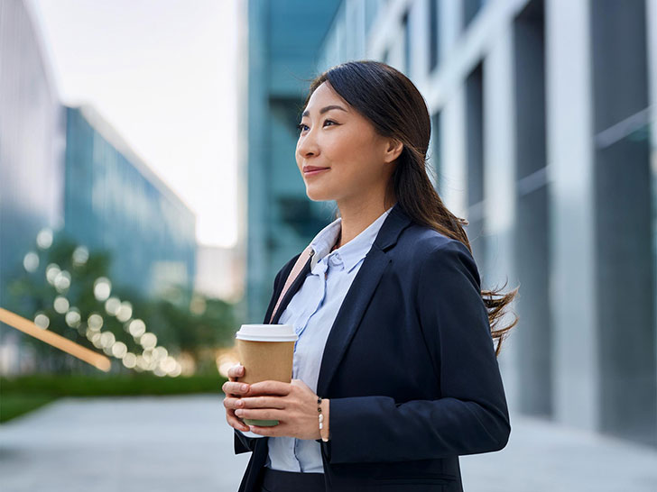 コーヒーを片手にオフィス街にたたずむ女性